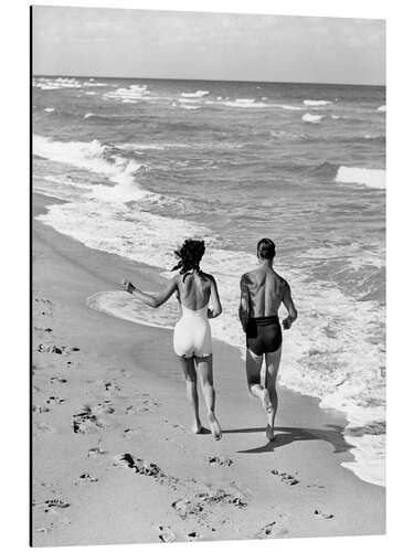 Aluminiumtavla Couple wearing jogging at edge of ocean beach, 1930's